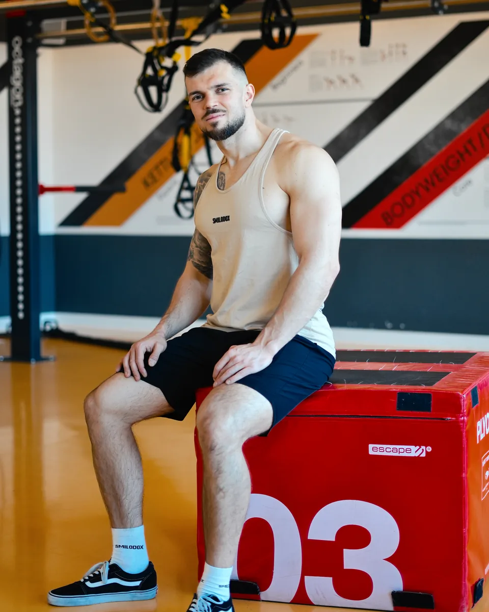 Adnan Lojic lächelnd auf einer Trainingsbox im Fitnessstudio